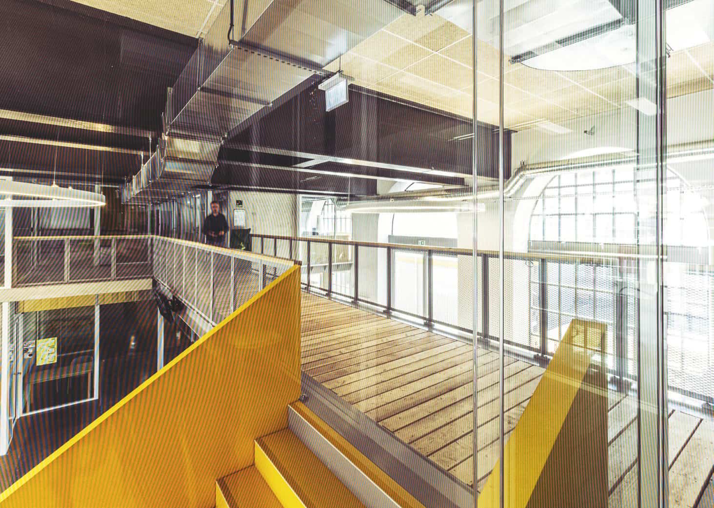Espace de coworking urbain avec design contemporain, murs en verre, escalier jaune et ambiance lumin.