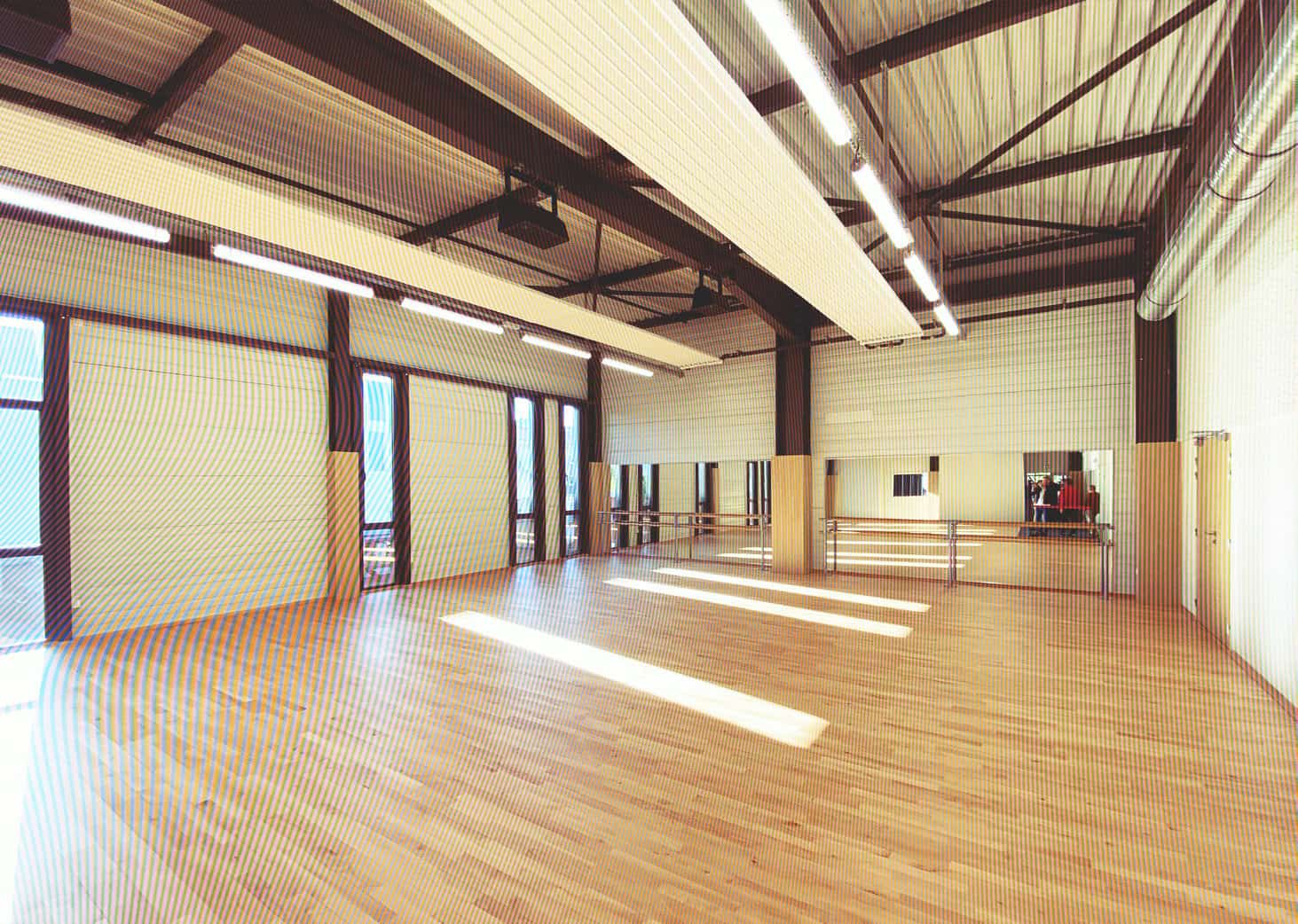 Espace de danse spacieux avec parquet en bois et murs en métal, idéal pour cours de danse et entraîn.