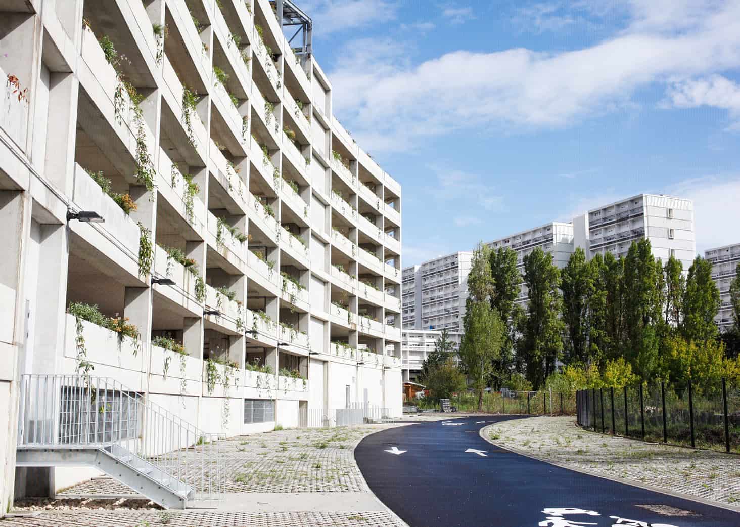 Balcon d'immeuble résidentiel urbain avec végétation et chemin piétonnier.