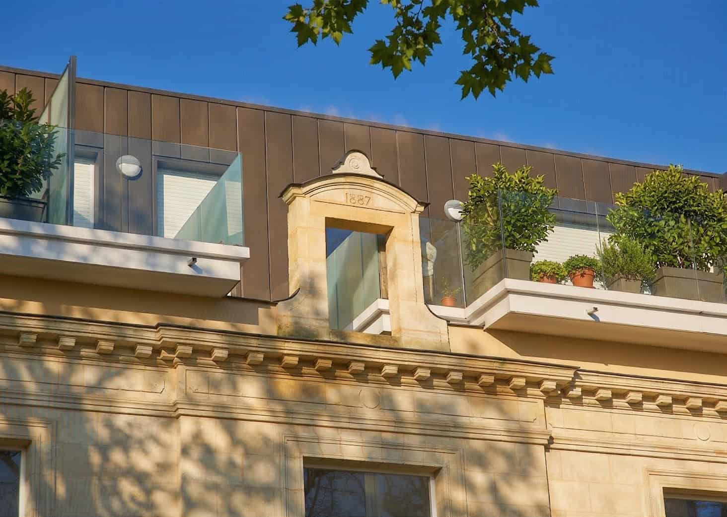 Balcon avec plantes et vue sur le ciel bleu, façade en pierre et design contemporain.