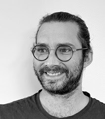 Homme souriant avec lunettes, représentant la créativité et l'innovation urbaine.
