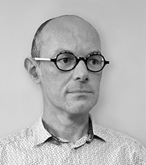 Portrait d'Urb1n avec lunettes, expression sérieuse, fond neutre.