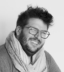 Homme souriant portant lunettes et écharpe, portrait en noir et blanc.