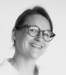 Portrait d'une femme souriante portant des lunettes, représentant confiance et professionnalisme.
