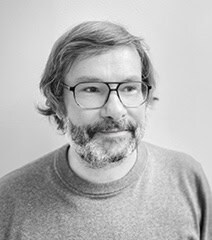Portrait d'un homme avec lunettes, barbe et cheveux gris, souriant, dans un style professionnel et c.